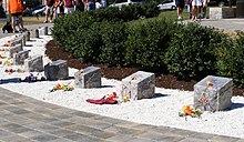 Blocks of stone arranged in a semi-circle in a bed of white gravel with a paved walkway in front and green bushes behind.