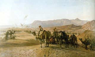 Et stort antal mænd der ridder på kameler i en bar ørken. Der er en by i baggrunden og nøgne stenede bjerge bagved.