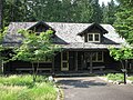 Photograph of the Hiker's Center, one of the Longmire Buildings at Mount Rainier National Park on a late spring day, a low, rustic, log building with a patch of long grass in front and deep green forest behind.