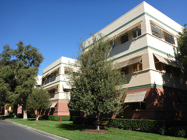 Three story building with green stripes surrounded by some trees
