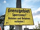 Yellow sign mounted on a pole reading "Grenzgebiet Sperrzone! Betreten und befehren verboten!"