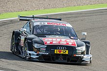 Voiture noire, vue de face, à l'amorce d'un virage, sur une piste sèche.