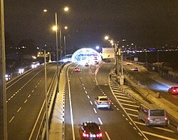 Two two lane roads depicted. At the bottom left, a car is travelling. At the bottom right, a van parked on diagonally-crossed marked no-entry section. Two lane road on the right splits into a tunnel and a single-lane exit.