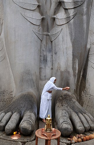 Последовательница джайнизма проводит ритуальное омовение (абхишека) Гоматешвары — статуи Бахубали в Шраванабелаголе, Карнатака