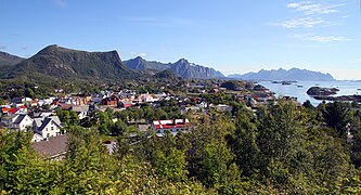 Foto einer an der Küste gelegenen Ortschaft, im Hintergrund Berge und Inseln