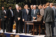 Рангел и еще около четырнадцати мужчин стоят вокруг стола, за которым президент Рональд Рейган подписывает законопроект.