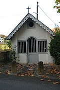 Vue d’un petit oratoire, maisonnette aux murs blancs et aux boiseries grises.