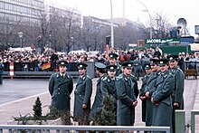 Police officers of the East German Volkspolizei wait for the official opening of the Brandenburg Gate of the Berlin Wall on 22 December 1989. Volkspolizei at the official opening of the Brandenburg Gate.jpg