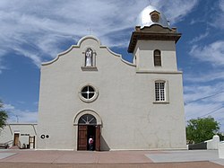 Фасад миссионерской церкви с белой лепниной снаружи с пристроенной колокольней справа и пристроенным портиком слева.