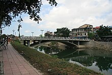 Небольшой бетонный мостик с подмостком через небольшой водоем. Это для пешеходов и фонари присутствуют. По сторонам от воды есть бетонная набережная, а на берегу проложена пешеходная дорожка с благоустроенной живой изгородью.