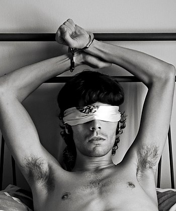English: A man handcuffed to a bed and blindfolded