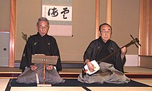 A Japanese man playing a shamisen while another sings
