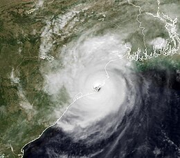 Image of a well-defined cyclone, with clouds appearing in off-white shades and land or water appearing as darker shades of gray. Rainbands are visible around the storm, and an eye is present as an area of darker shading at the storm's center.