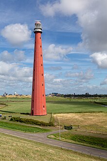 A tall red lighthouse in a field along a small road