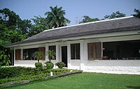 a single story white building with a grey roof and palm trees in the background