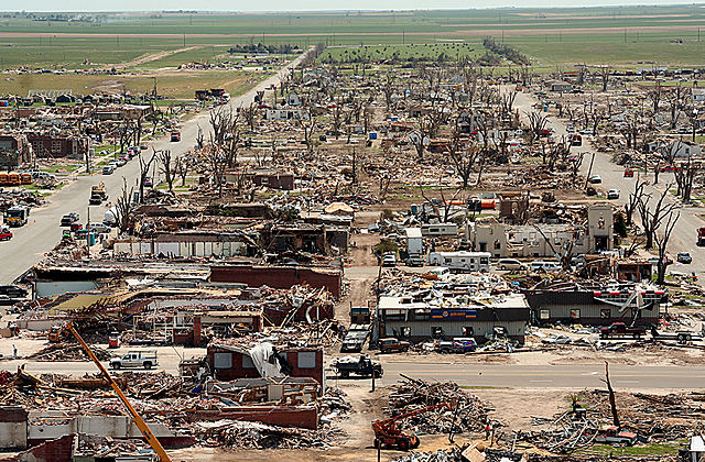 An aerial photograph of a town with all of the homes largely destroyed. Trees are stripped of their leaves or reduced to just their trunks.