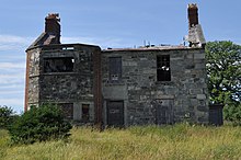 The ruins of a stone and brick building, with a projecting bay window on the left side of the facade.