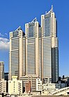 Mid-level view of a white, window-dotted, rectangular high-rise; the corners are cut and made of glass