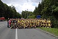 Un groupe de cyclistes vêtus de jaune pose sur une route, devant le panneau signifiant l’entrée sur le territoire français.