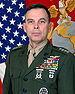 A color image of William Nyland, a white male in his Marine Corps Service A uniform. He is not wearing a hat, several ribbons are visible as well as a round badge, rifle and pistol marksmanship badges and naval aviator insignia. The Marine Corps flag and United States flag are visible in the background.