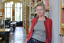 Anke Berghaus-Sprengel steht an ein Bücherregal gelehnt in einem Lesesaal.