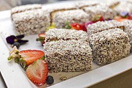 Lamingtons on a plate. Each rectangular portion is completely coated on all sides by shredded coconut