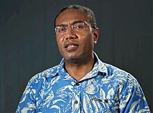 Pete Kenilorea Jr. 2018. Porträt eines jungn Mannes mit kurzem Kraushaar und Brille in einem Hawai-Hemd.