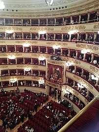 Salle de spectacle avec parterre de fauteuils entouré par six galeries ; à l'extrémité, un passage ouvert surplombé par une riche loge et seulement trois galeries.