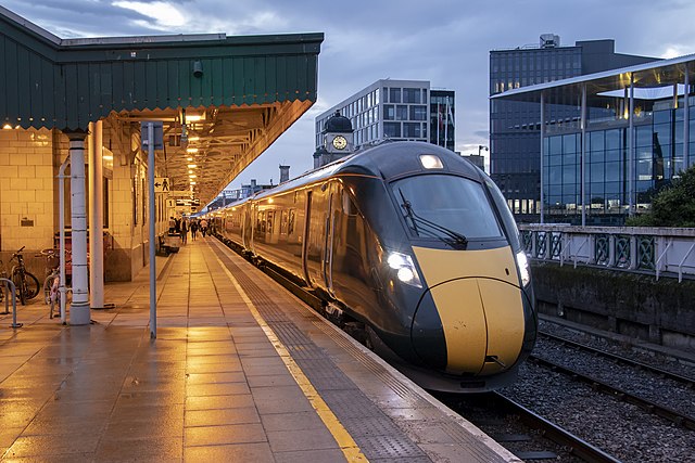 Sleek-looking inter city train curving away to the right on a station platform with modern buildings to the right