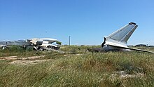 débris d'un avion sur un terrain courvert d'herbes folles.