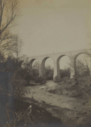 Photographie en sépia d'un cours d'eau serpentant et passant sous l'arche du pont.