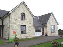 An image of Dihewyd School, showing a small building with some painted flowers on the walls and garden furniture outside