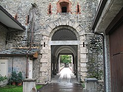 At the center of the photo is a stone archway leading into a short covered hallway that lets out on the other side of the building. The building itself is a mix of smooth, worn-down gray stone and larger, more visible stones. The windows are fortified with red-brown brick.