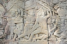 A Khmer soldier (left) fights against his Cham rival (right). The bas-reliefs of the Bayon, always depict the Chams as wearing helmets in the shape of a Magnolia champaca flower. Bas-reliefs du Bayon (Angkor) (6912550571).jpg