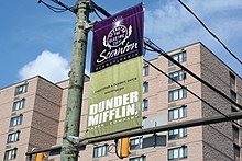 Photographie d'une bannière de rue sur laquelle on peut lire « Scranton » et « Dunder Mifflin ».