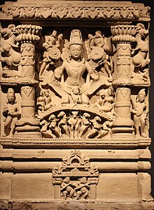 Surya (center) is typically depicted holding lotus flowers and riding in a horse-drawn chariot. He is accompanied by his wives (bottom female figures) and children (other male figures). The dawn goddesses (top female figures) are depicted shooting arrows. Circa 9th century CE. Lord Surya.JPG