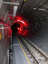 Round concrete tunnel with railway tracks on the bottom, an emergency escape walkway on the left, and various wires and pipes running along the tunnel wall.