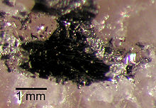 A dark mass, approximately 2 millimetres in diameter, on a rose-coloured crystal substrate