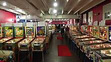 Most of the pinball machines are lit up and ready to play, except for a couple with the playing field opened up for repairs. Informative signs stand on top of each machine, describing its history and importance. It's night and attendance at the museum is relatively light.