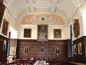 A wood-panelled hall, with a large portrait of Elizabeth I in the middle of the far wall; other portraits alongside and around the walls; a white plaster ceiling with light blue decoration