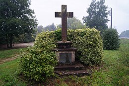 Photographie en couleurs d'une croix commémorative en pierre, entourée d'un buisson.