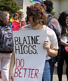 Image of a student holding a sign reading "Blaine Higgs, do better" at a rally