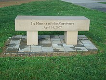 Bench engraved with "In Honor of the Survivors" and "April 16, 2007" standing on an area of pavement blocks surrounded by grass.