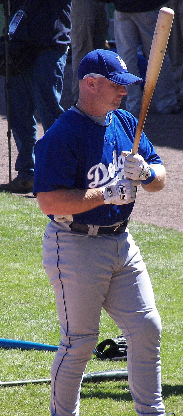 A man wearing a blue baseball jersey and cap holding a baseball bat in his two hands