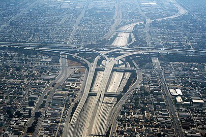 Photographie aérienne centrée sur un énorme échangeur autoroutier implanté au cœur d'une immense banlieue exclusivement résidentielle.