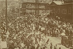 Photographies depuis l'étage d'une maison d'une rue pleine de manifestants, entourée de bâtiments en bois.