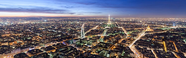 Nachtaufnahme vom beleuchteten Paris mit dem Eiffelturm und dem Pantheon auf der rechten Seite. Der blau-violette Himmel hat links die gelben Reststreifen der untergehenden Sonne und rechts einen weißen Lichtstreifen.