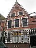 Huis met brede trapgevel van het zgn. Haarlemse type rijk met natuurstenen blokken versierd; pui aangepast. Met tongewelf gedekte gang