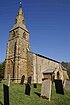 A stone church with a tiled roof; on the left is a tower with a tall spire, and the body of the church extends to the right