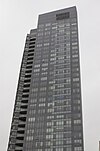 Вид с земли на современный 40-этажный небоскреб с цельностеклянным фасадом в серых тонах.